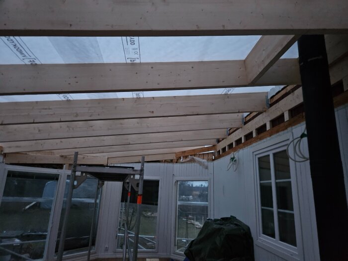 Träbjälkar och stomme i under konstruktion av tak över inglasat uterum; före installation av plåt, isolering och innertak.