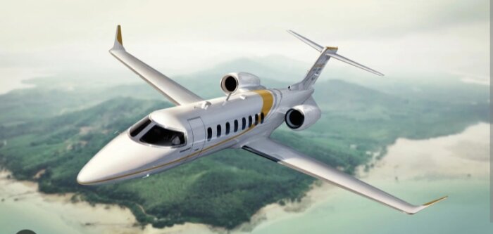 Ett elegant privatjet med två motorer flyger över en grönskande ö och kustlinje, med en grön och blå färgton på landskapet nedanför.