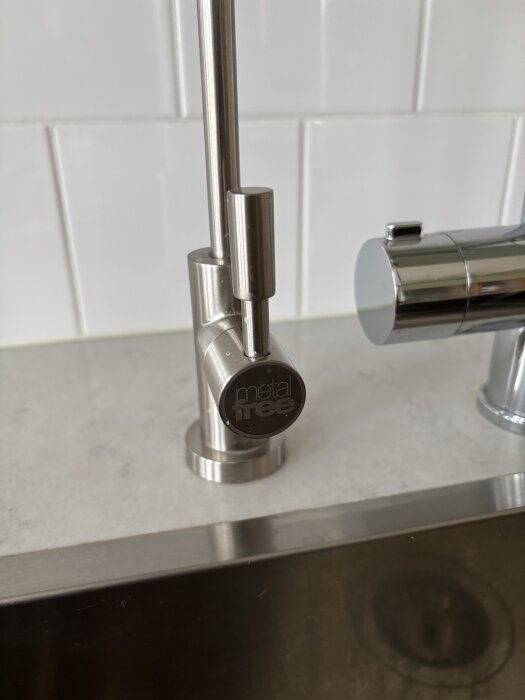 Metallisk diskmedelspump monterad på köksbänk av marmor, bredvid en kran. Pumpen är märkt med texten "metal free".