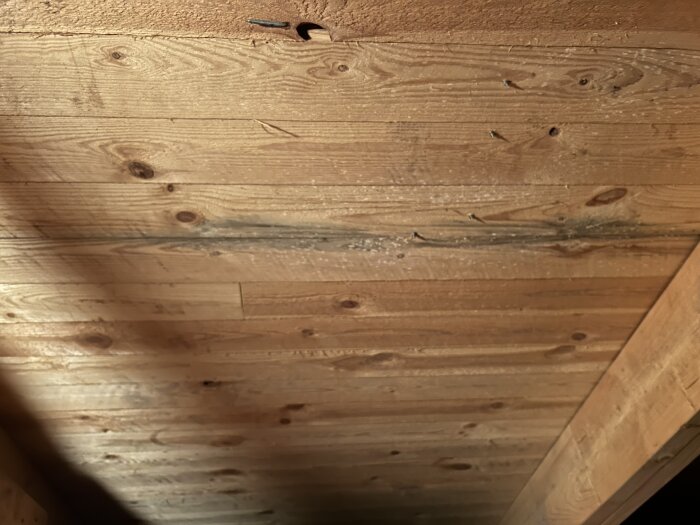 Trätak med synliga kvistar och några skruvar, delvis skuggat i ett byggprojekt.