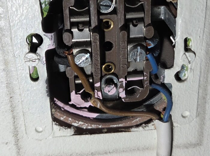 Elektrisk anslutning med kablar och klämmor, delvis målad, i en oregelbunden installation, synlig bakom ett element enligt sammanhanget.