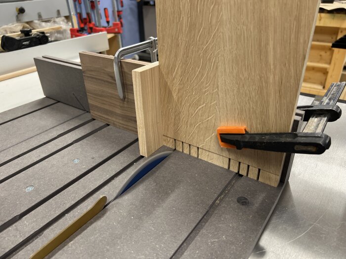 Trästycke fastklämt vid kapsåg för att skapa tappar, med flera markerade snittlinjer och en orange klämma för fixering.