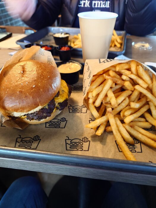 Hamburgare med smält ost och pommes frites serverade på en bricka med dipp.
