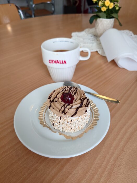 Gräddtårta dekorerad med körsbär och choklad, serverad med kaffe i en Gevalia-kopp på ett cafébord.