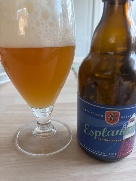 Ölglas med skummande lager och flaska märkt "Esplanad" på ett bord.