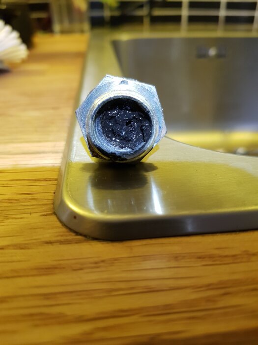 Korroderat rör med svarta avlagringar, troligtvis påverkat av olika vattenkällor i värmesystemet över tid, på köksbänk vid diskho.