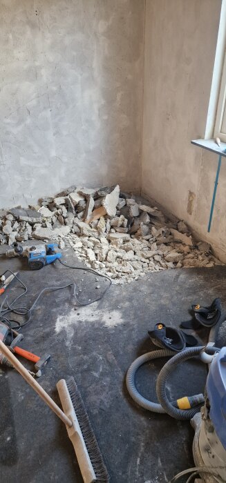 Rivningsarbete med betongbitar på golvet, borr och verktyg i rummet, antydande pågående renovering.
