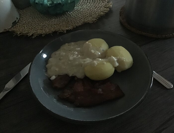 Tallrik med stekt fläsk, löksås och kokt potatis på mörkt bord.