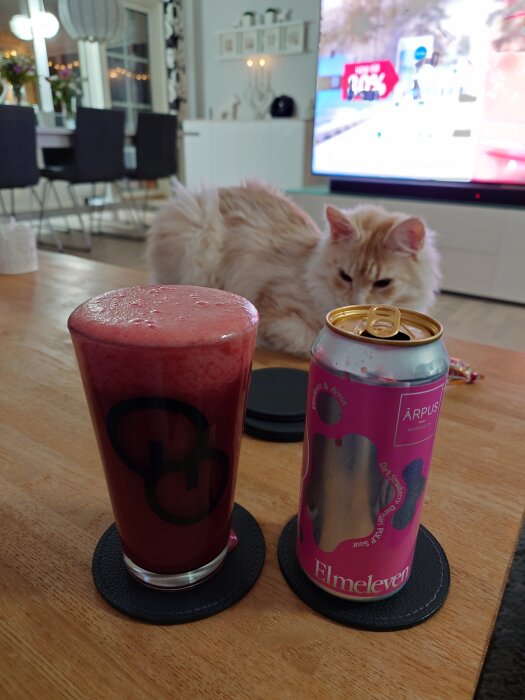 En ölburk med rosa etikett från Elmeleven och ett glas syrlig öl på ett bord, med en katt i bakgrunden.