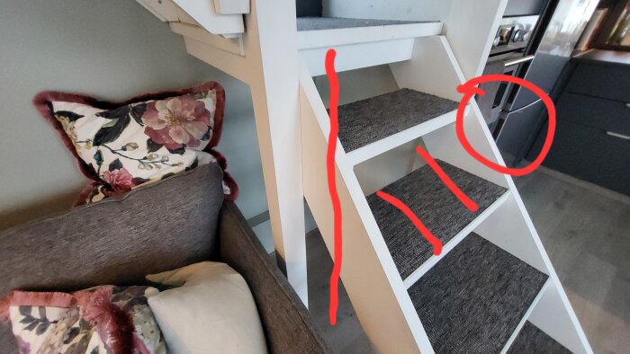 Vit trappa med tre steg täckta av grå matta; röd linje och cirkel markerar mått på undersidan; kuddar och soffa bredvid trappan.