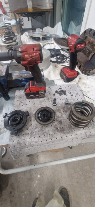 Verktygsbänk med två röda skruvdragare, spiralfjäder och metallkomponenter på en perforerad duk.