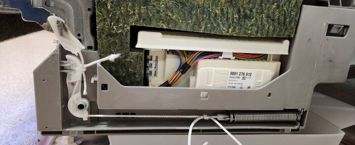 Detalj av diskmaskinens insida med skarvad nylonlina och fjädermekanik synlig, kabeldragning och komponenter i bakgrunden.