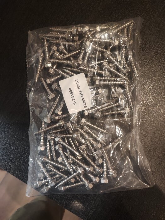 Påsen innehåller rostfria skruvar märkta S-TS1000, storlek 6x30mm, med en etikett som anger 100 skruvar per sats.