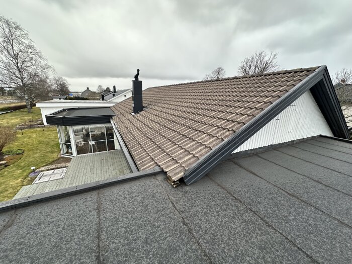 Bilden visar ett hus med tegelpannor på taket, en skorsten och ett äldre utseende med trädgård och uteplats i förgrunden.