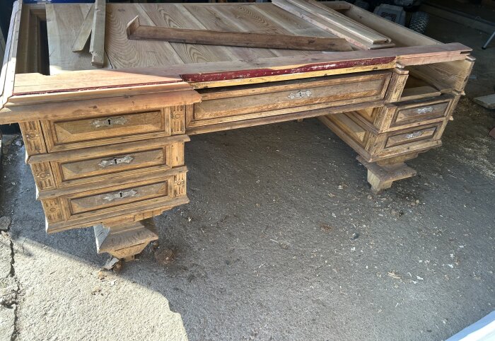 Gammalt skrivbord under renovering med flera lådor och synlig trälåda; skadade kanter och lådhandtag i metall.