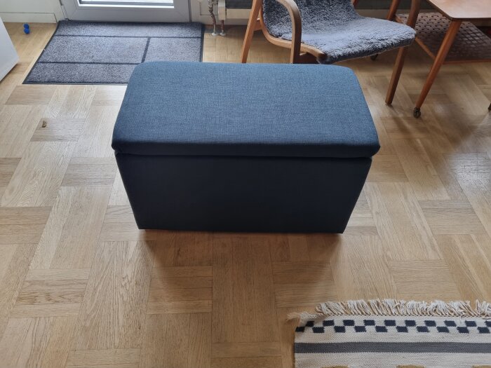 En måttanpassad sittpuff i blått tyg för förvaring av hantlar, placerad på ett parkettgolv i ett vardagsrum.