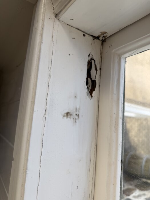 Fönsterbrädan på verandan med sprickor och murken träyta, visar del av ett gammalt glasfönster.