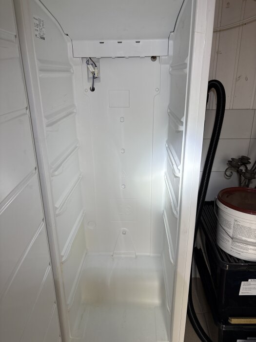 Inre av en Electrolux frys med borttagen bakre skiva, exponerade elkablar och kåpa som sitter fast ovanför ett kopparrör.