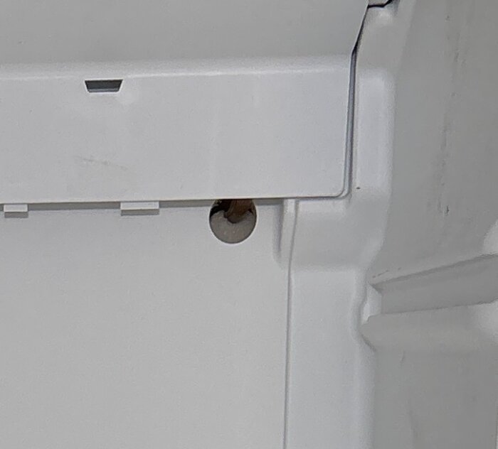Närbild på insidan av en Electrolux-frys med avlägsnad bakskiva, visar område runt avrinningen med synligt kopparrör under en vit kåpa.