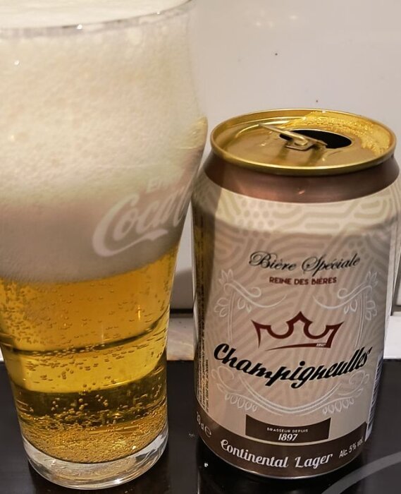 En ölburk med texten "Champigneulles" bredvid ett fyllt ölglas med skum på toppen.