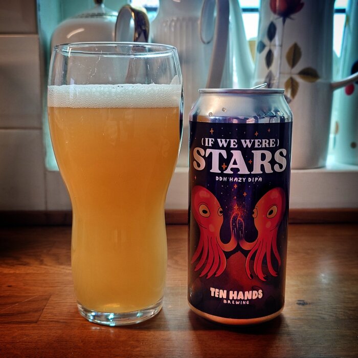 Glas med öl bredvid en burk märkt "If We Were Stars", DDH Hazy DIPA från Ten Hands Brewing, på ett träbord i köksmiljö.