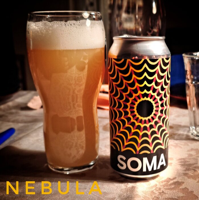 Glas med skummande gul dryck bredvid en färgglad burk märkt "SOMA" på ett bord.
