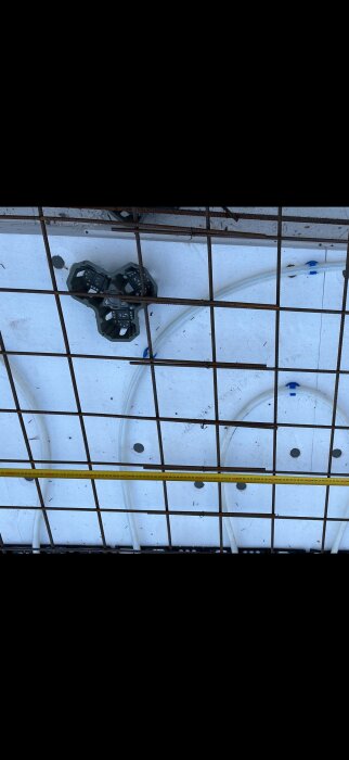 Betongförberedelse med armeringsjärn och golvvärmerör på plats. Ett plastfäste syns också på bilden.