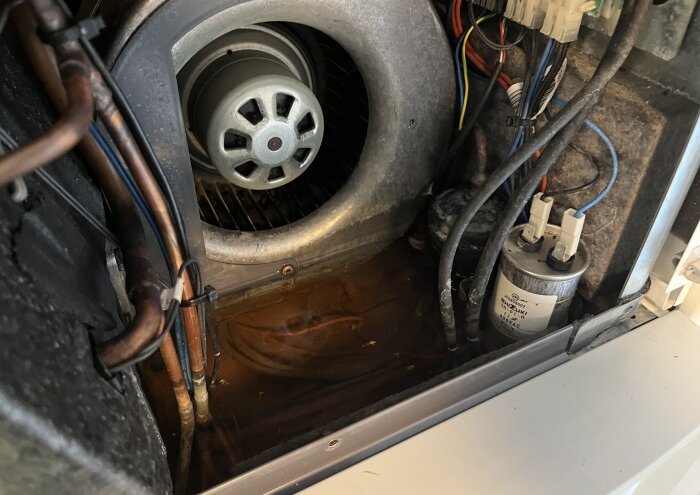 Interiör av en Nibe F730 med synlig fläkt och vattenansamling vid basen, omgiven av rör och ledningar.