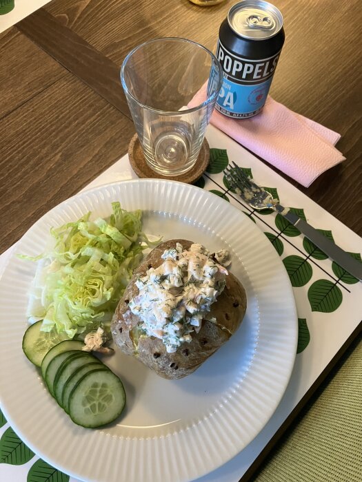 Bakad potatis med Skagenröra och sallad på tallrik, glas och IPA-burk på bord.
