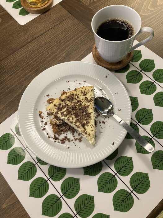 Citroncheesecake med riven choklad på en tallrik, serverad med kaffe på en grönmönstrad bordstablett.