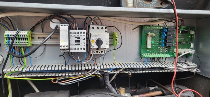 Elektrisk kopplingspanel med kablar och komponenter, inklusive en svag gul markering som visar hetgasgivarens position.