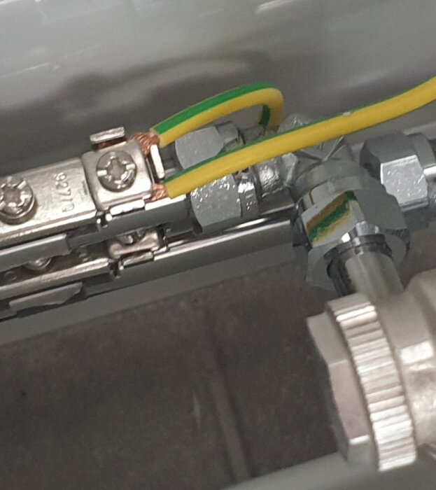 Synlig koppartråd och gulgrön ledning vid handdukstork i badrum, nära fönster. Fråga om elsäker installation och kabelisolering.