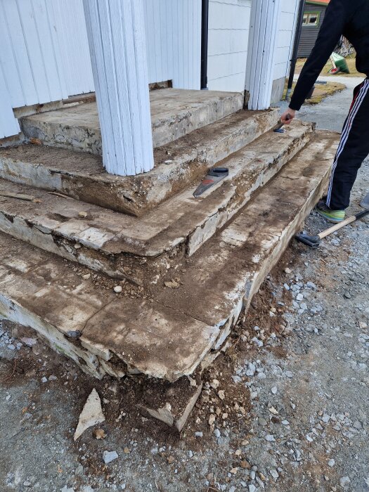 Skör och eroderad betongtrappa med synlig sand och stenar, någon inspekterar med verktyg i handen.