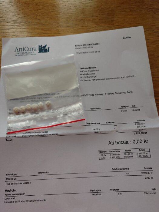 Kvitto från AniCura med medicin och en plastpåse med tabletter på ett träbord. Totalsumman är 0 kr att betala.