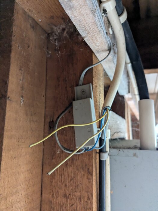 Tunn grå och svart kabel i garage, anslutna med plastplint. Kabeln leds genom väggen och ned i golvet, åtföljd av två exponerade tunna gulgröna ledningar.