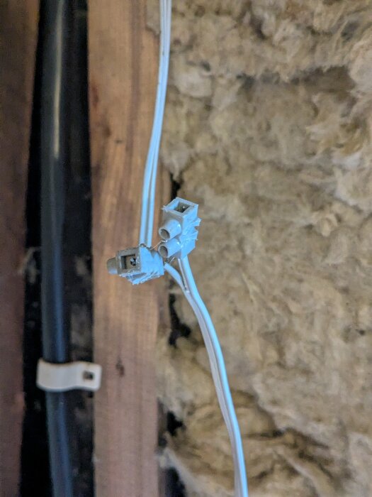 Närbild av två elektriska snabblåsanslutningar på vita kablar mot bakgrund av isolering och trä.