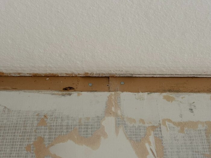 Vägg vid tak med synliga skruvar och ojämn tapet, del av pågående renovering i ett radhus från 1967.