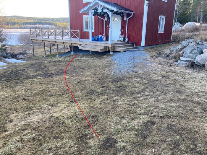 Bild av gräsmatta framför ett hus med en röd linje markerad som planerad placering för stödmur. Stenarna syns till höger.
