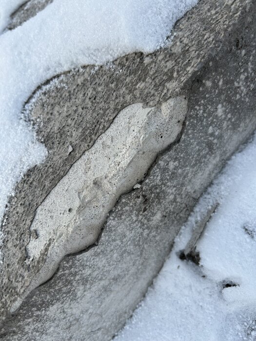 Betongtrappa med skadad yta delvis täckt av snö, med synliga sprickor och ytslitage.
