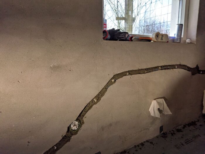 Vägg med grundad puts och glasfibernät runt elinstallation, fönsterbräda med verktyg. Grov struktur av ny puts synlig.