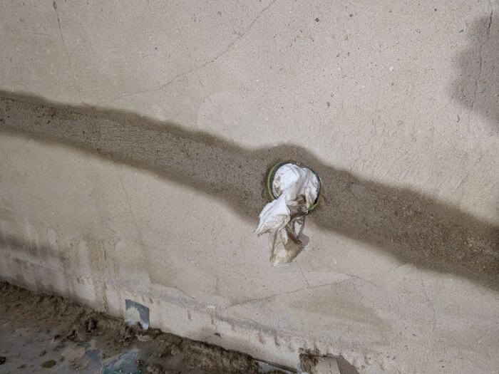 Murad vägg med grövre putsstruktur och glasfibernät; en del av väggen har grundningsbruk och murbruk applicerat. Synligt rör med papper.