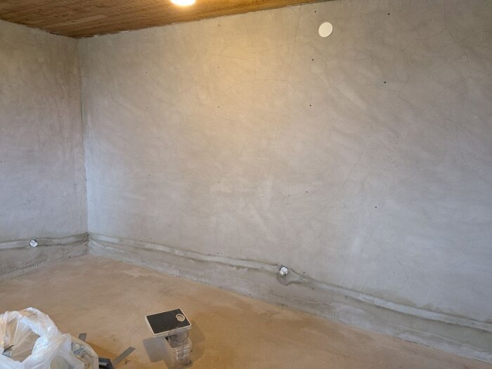 Nylagd putsning av väggar i ett rum med grövre struktur, glasfibernät, grundningsbruk och murbruk synliga, väntandes på fortsatt arbete.