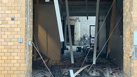 Förstörelse i en trappuppgång med hängande takplattor och bråte på golvet efter en explosion i en tegelbyggnad.