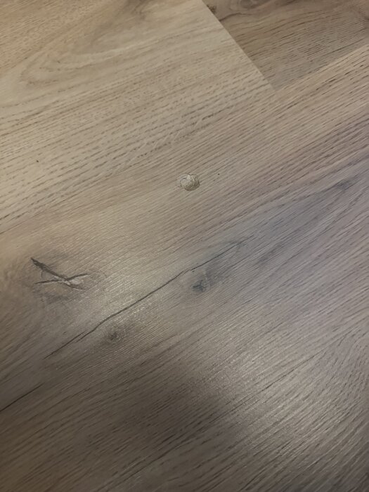 Laminatgolv med ett runt jack i ytan, visar behovet av reparation eller åtgärd.