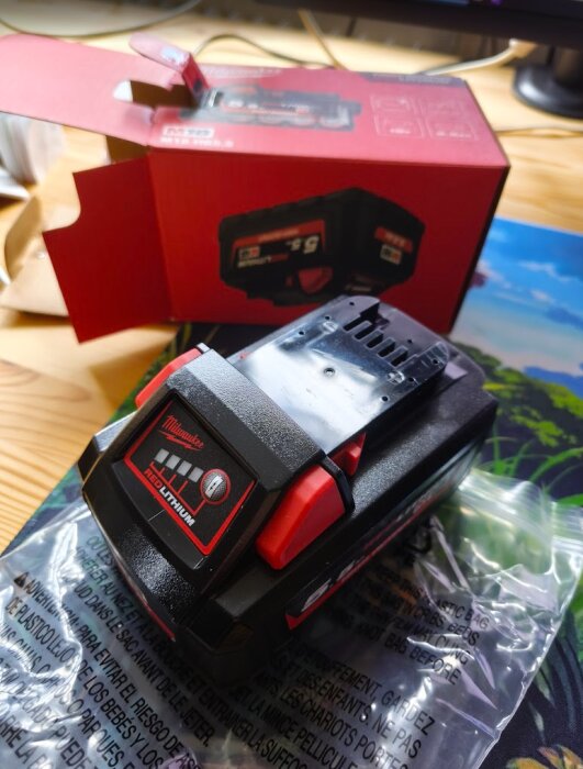 Milwaukee REDLITHIUM batteri och röd förpackning på ett bord.