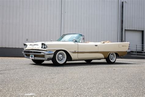 Klassisk vit och beige DeSoto cabriolet parkerad framför en stor byggnad. Modellen är vintage och kan vara värdefull för samlare.