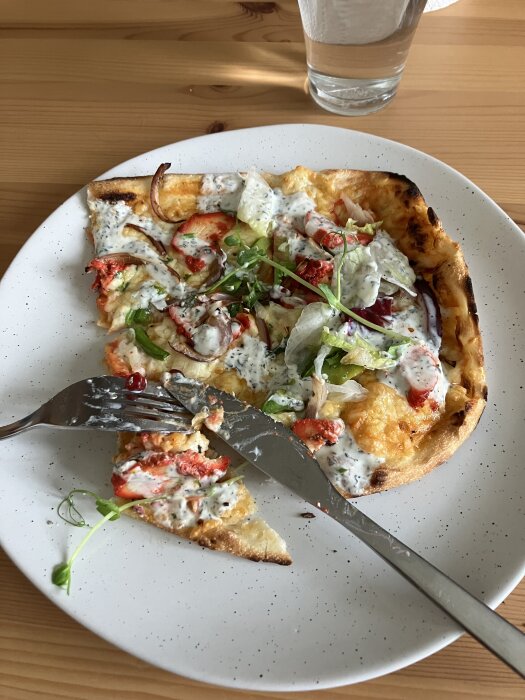Indisk pizza på tallrik med naanbröd, tandoorikyckling, färskost, paprika, rödlök och sallad.