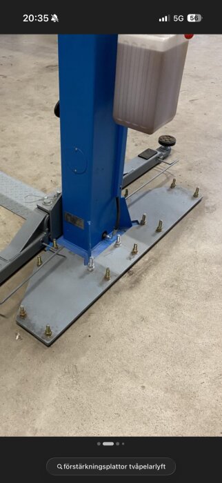 Förstärkningsplatta med bultar monterad på golv, används för att stabilisera en tvåpelarlyft i ett garage eller verkstad.