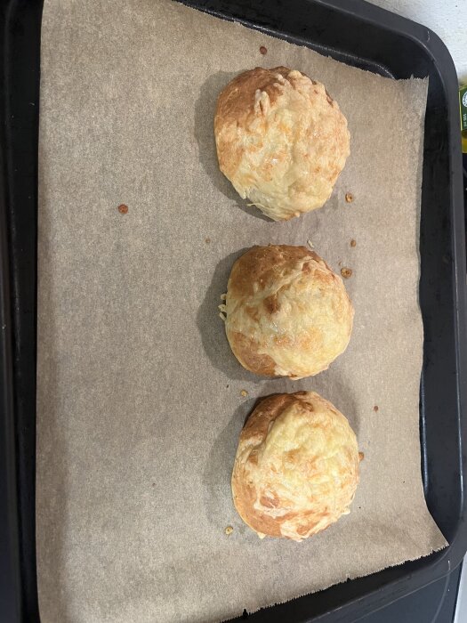 Tre frallor med smält ost ovanpå, placerade på bakplåtspapper i en ugnsform.
