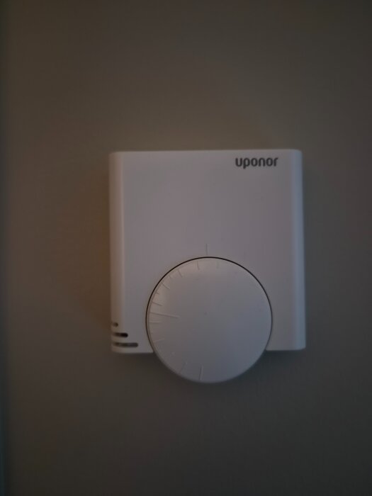 Uponor trådlös termostat t-55 monterad på en vägg, vit med en stor vridbar ratt och Uponor-logga i hörnet.